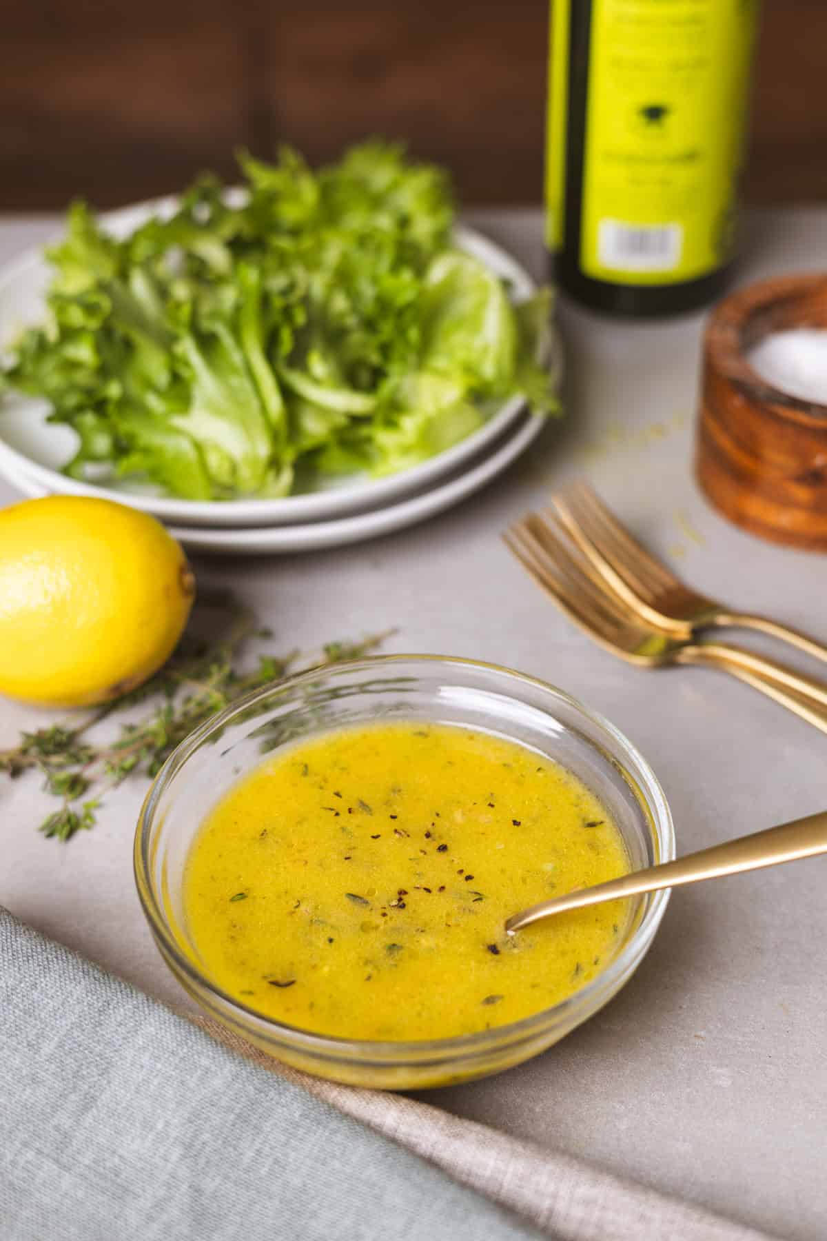 Lemon thyme vinaigrette on a gray table with a bowl of salad in the background.
