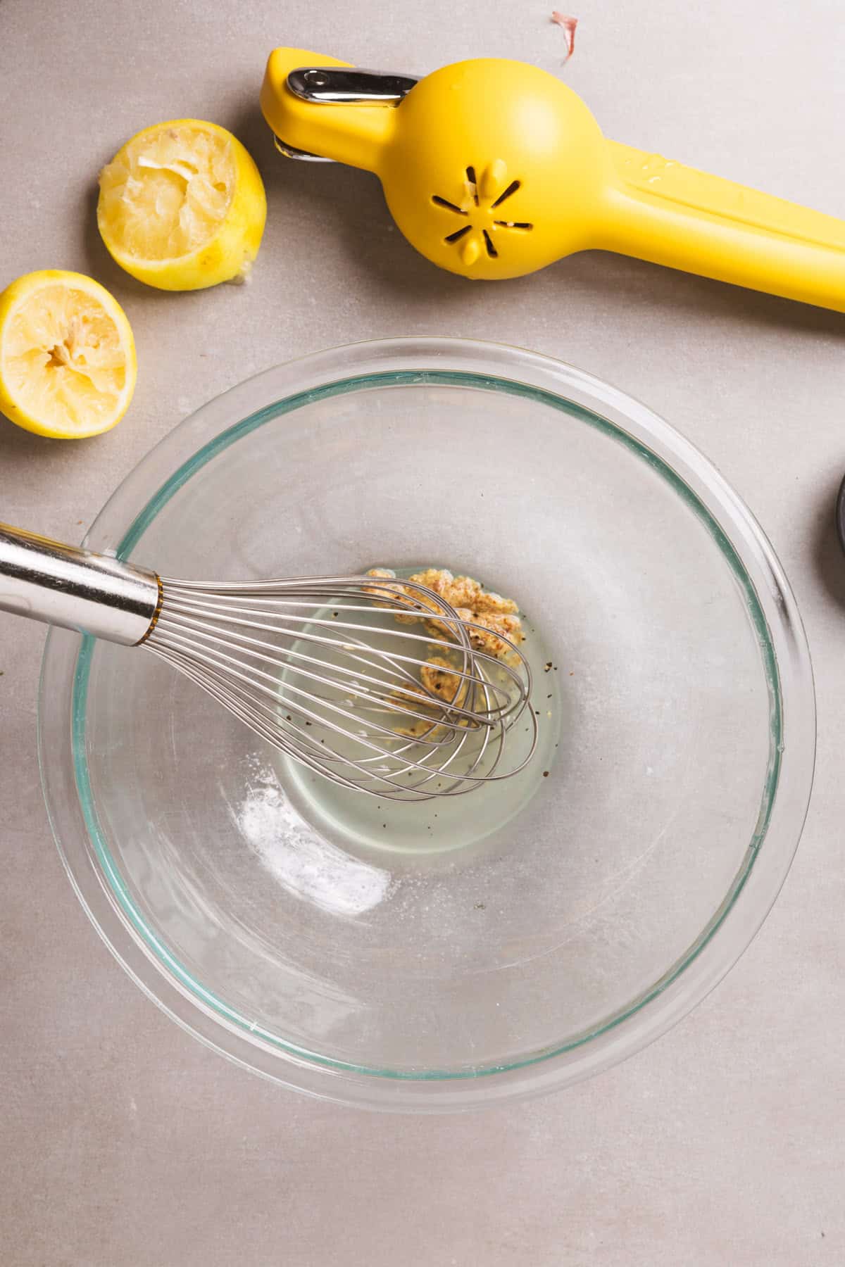 Mustard and lemon juice getting whisked together in a medium glass bowl. 