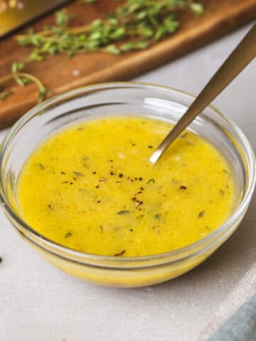 A close-up of lemon thyme vinaigrette in a glass bowl with a spoon inside.