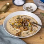 A close up of a white bowl with mushroom and leek soup on a butcherblock table.