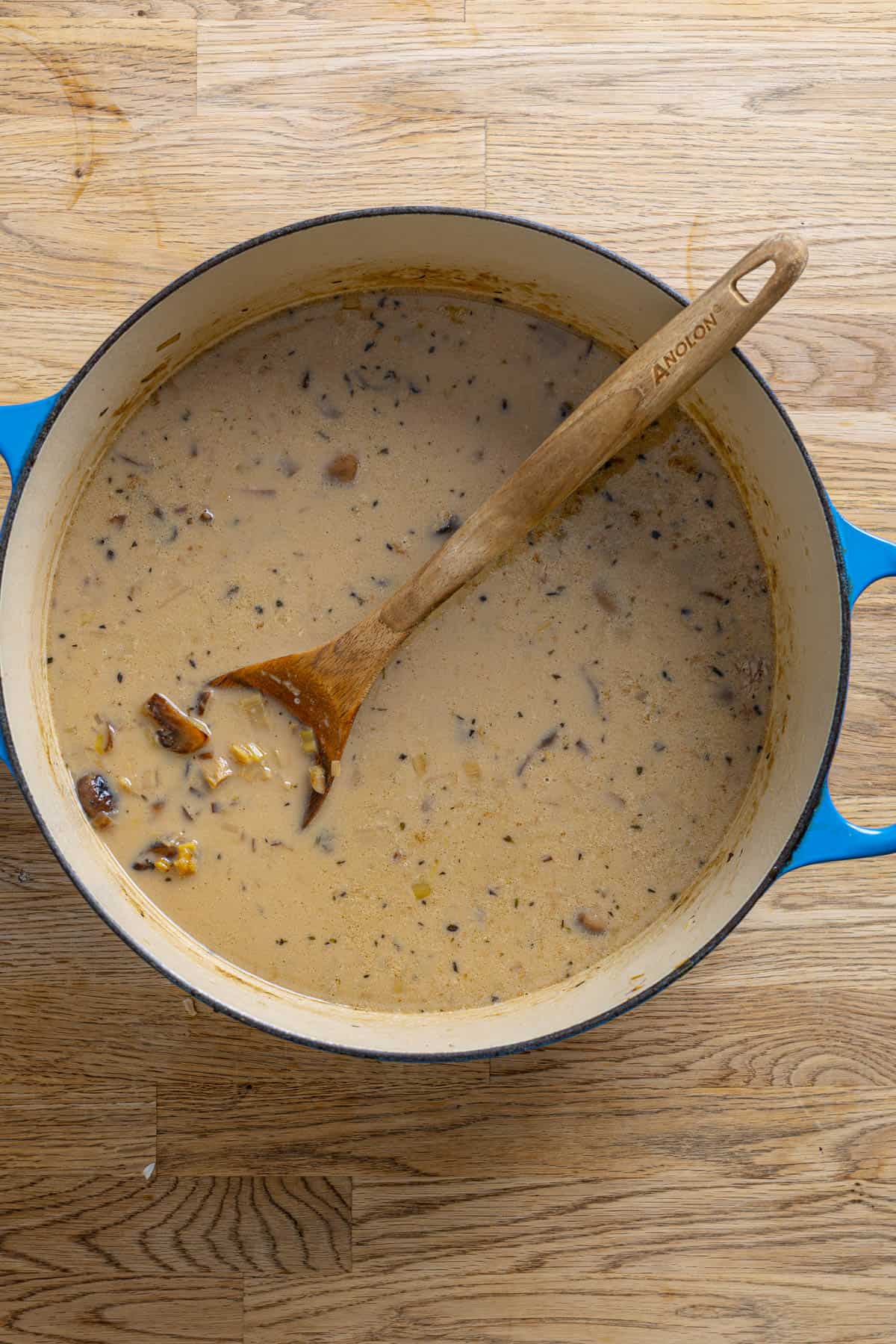 A dutch oven with mushroom leek soup on a butcher block counter.