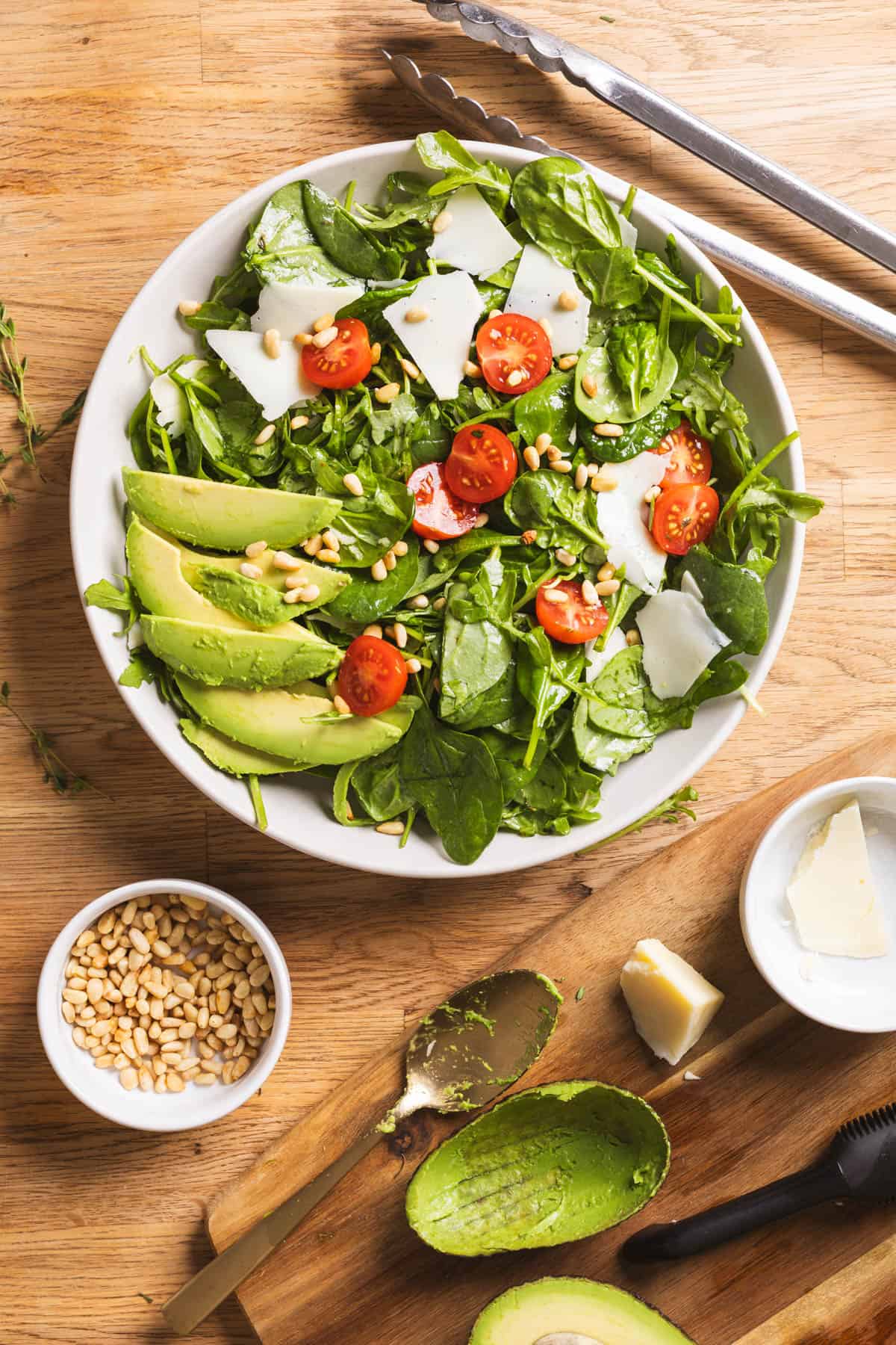 A serving bowl of spinach and arugula salad with a lemon thyme vinaigrette on a butcherblock countertop.