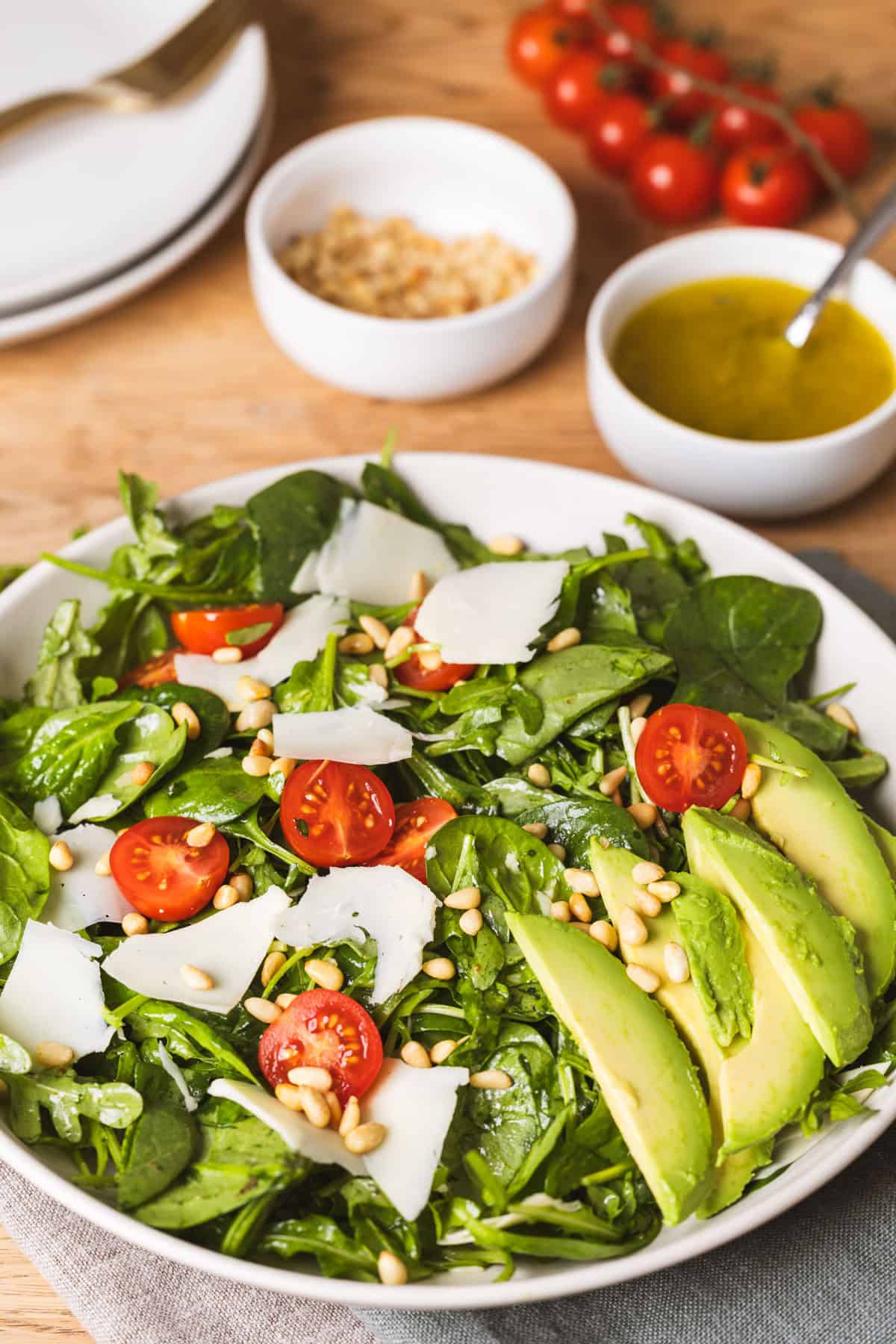 A large serving bowl with an arugula and spinach salad topped with tomatoes, pine nuts, and cheese.