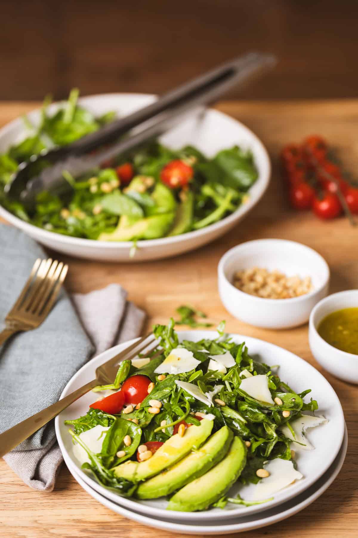 A table with a serving of spinach and arugula salad with a larger bowl in the background.