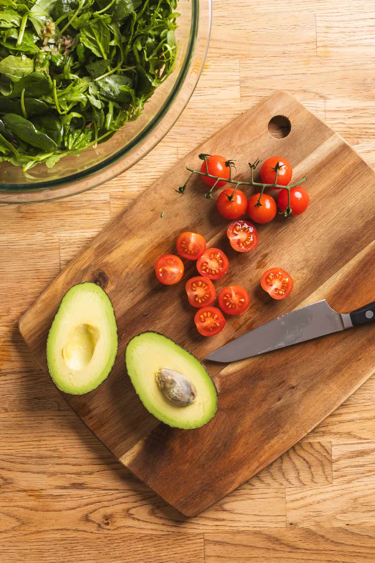 Tomatoes and avocado getting prepped for a spinach and arugula salad.