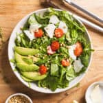 A serving bowl of spinach and arugula salad with a lemon thyme vinaigrette on a butcherblock countertop.