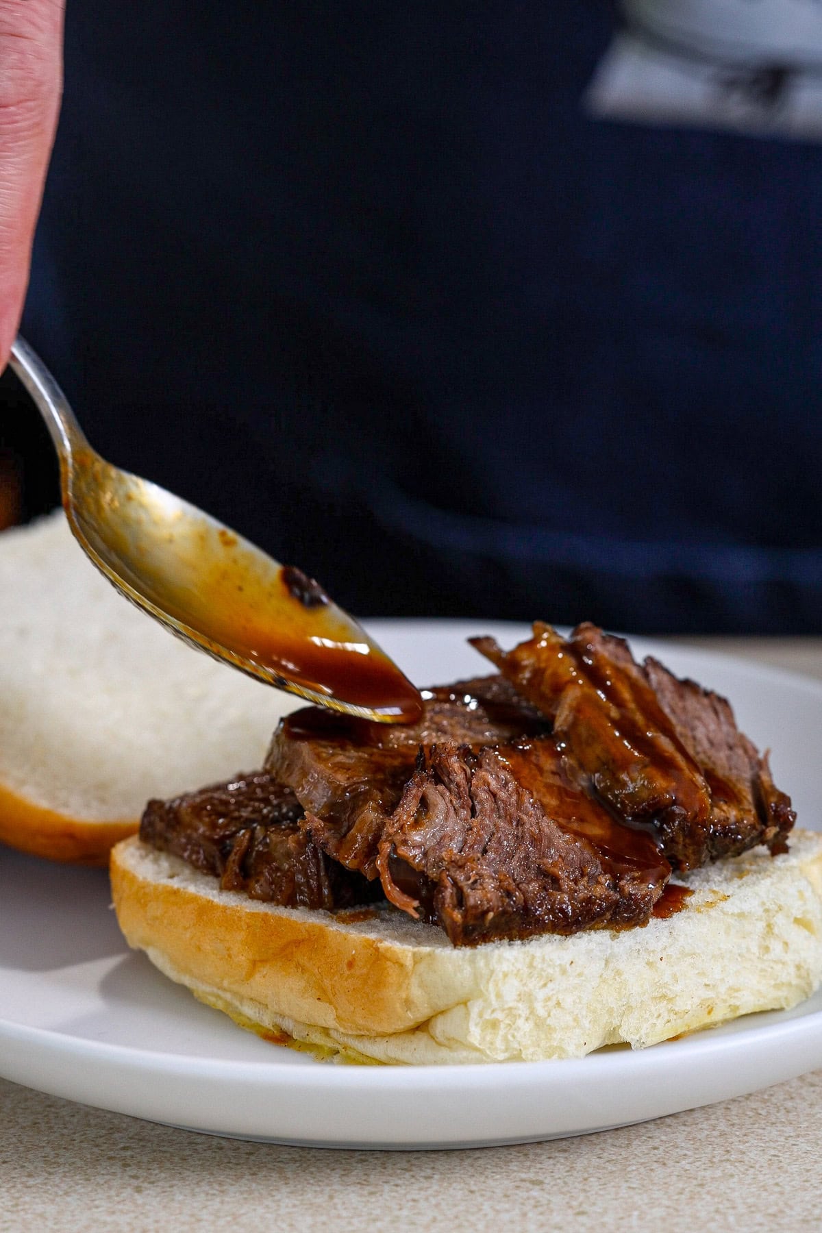 A rich sauce getting spooned over braised beef sliders.