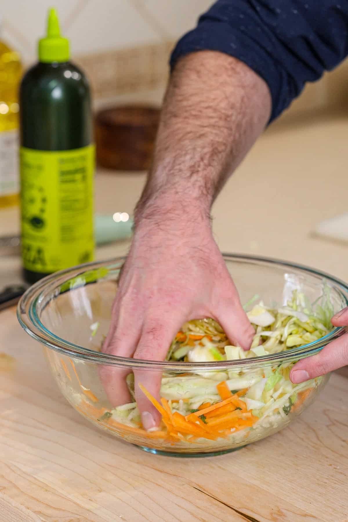 A hand mixing a cabbage and carrots for a citrus slaw.