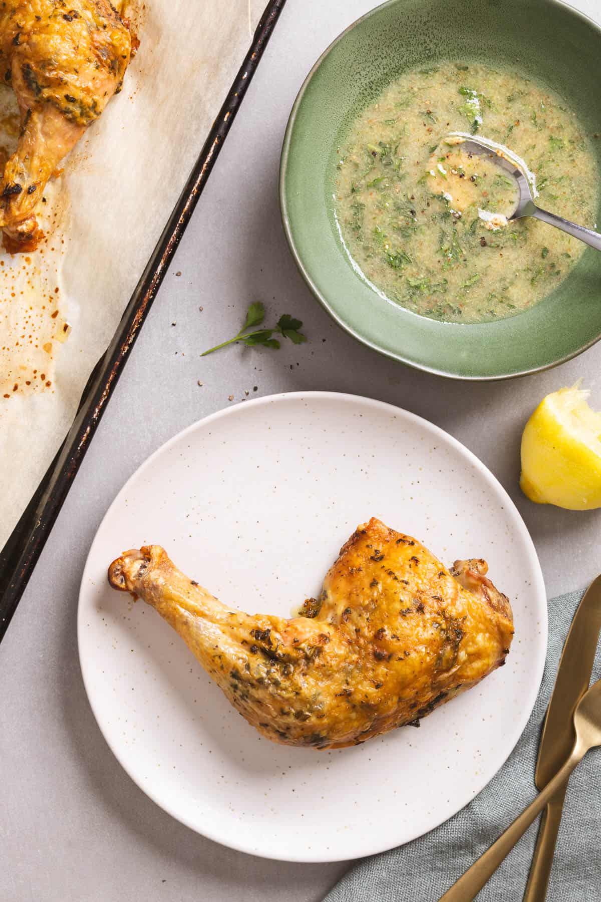 Roasted chicken leg quarter on a white plate with sauce in a small bowl to the side.