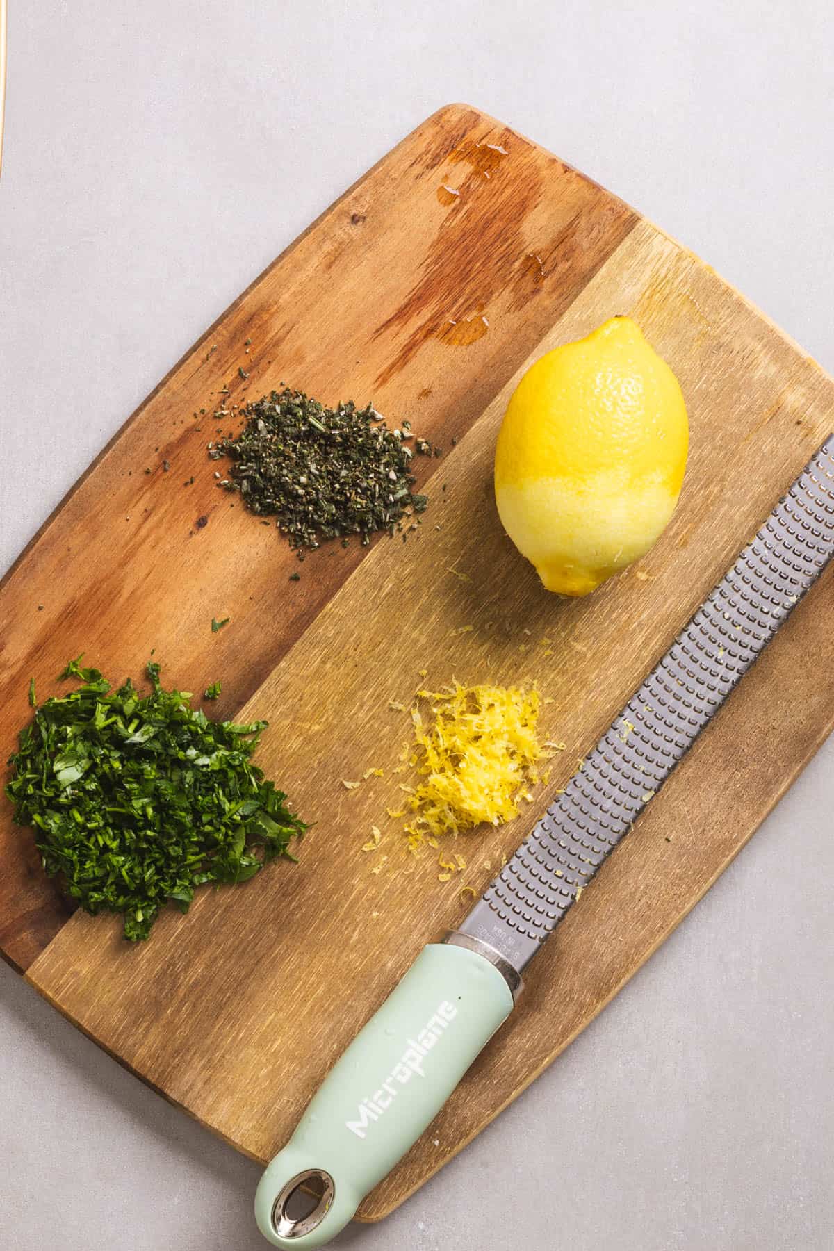 Herbs and lemon zest on a cutting board for a herb-lemon chicken marinade.
