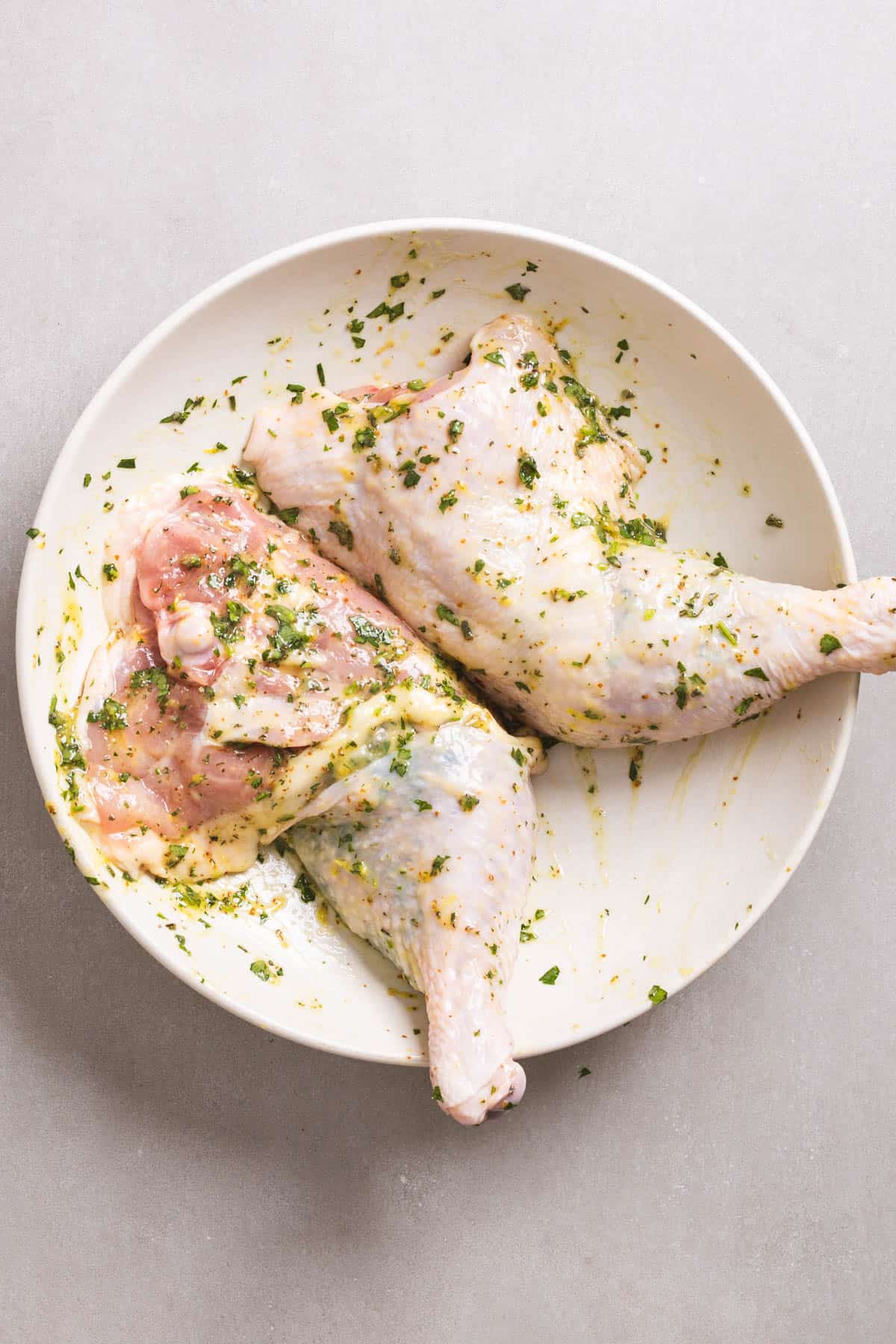 Chicken leg quarters in a large mixing bowl coated in an herb and lemon marinade.