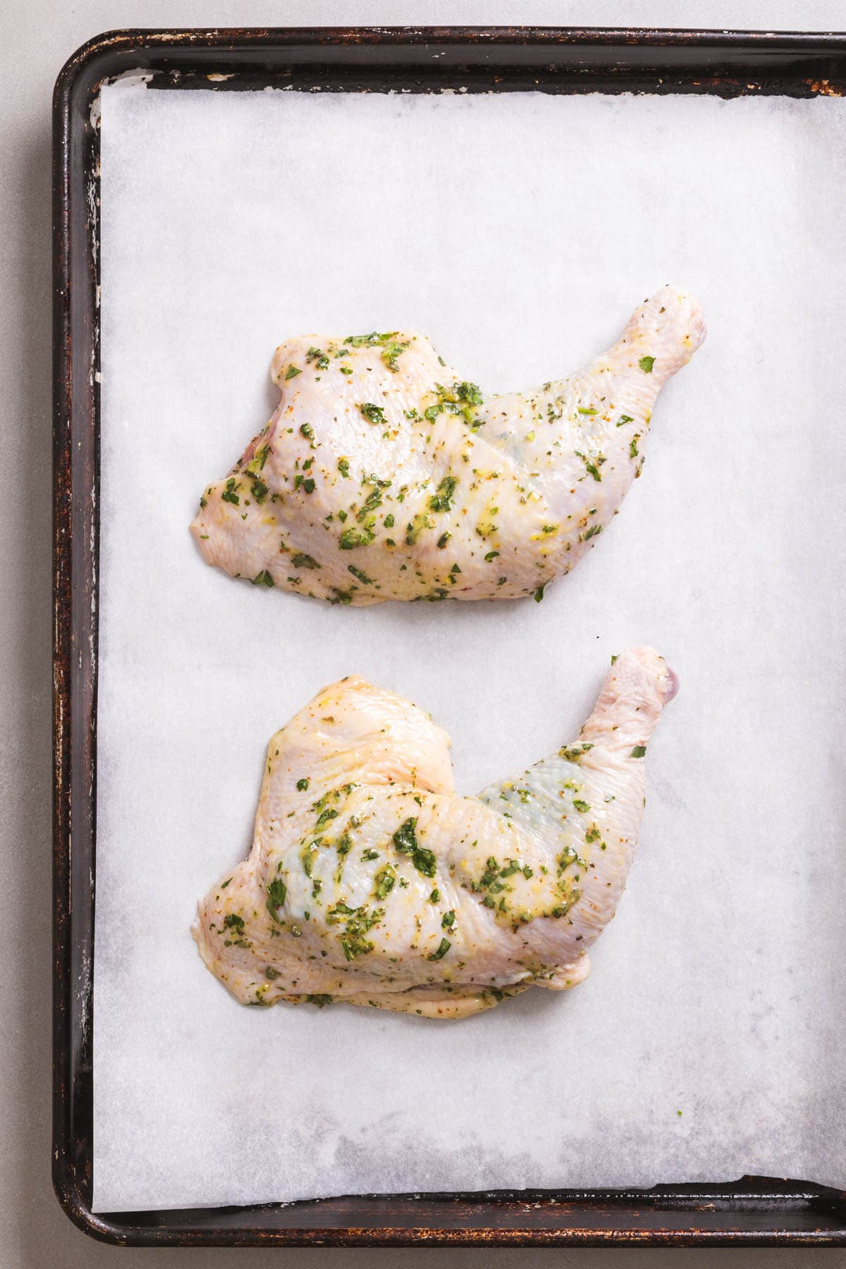 A baking sheet lined with parchment paper with herb marinated chicken leg quarters on top.