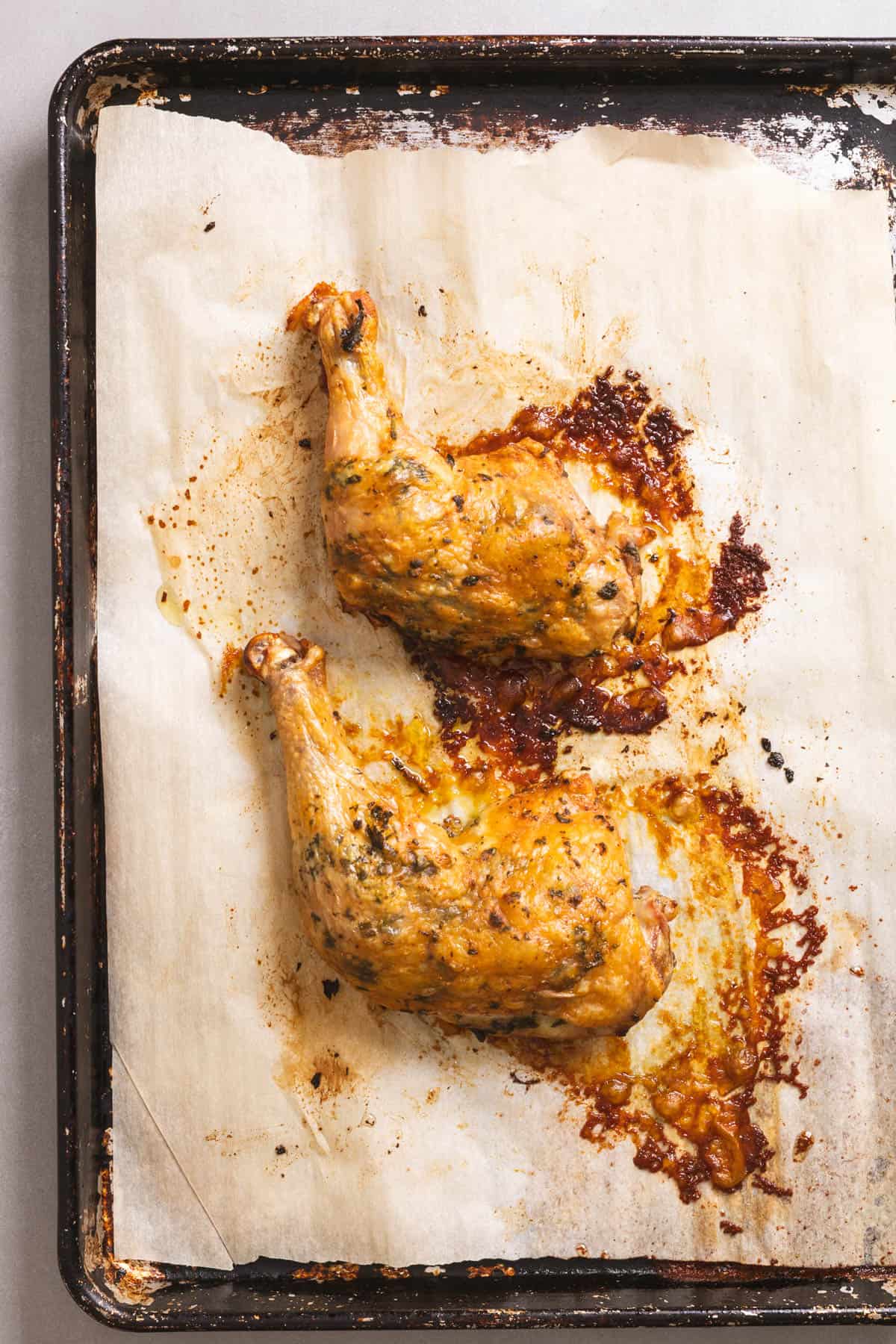 Herb roasted chicken leg quarters on a parchment-lined baking sheet.