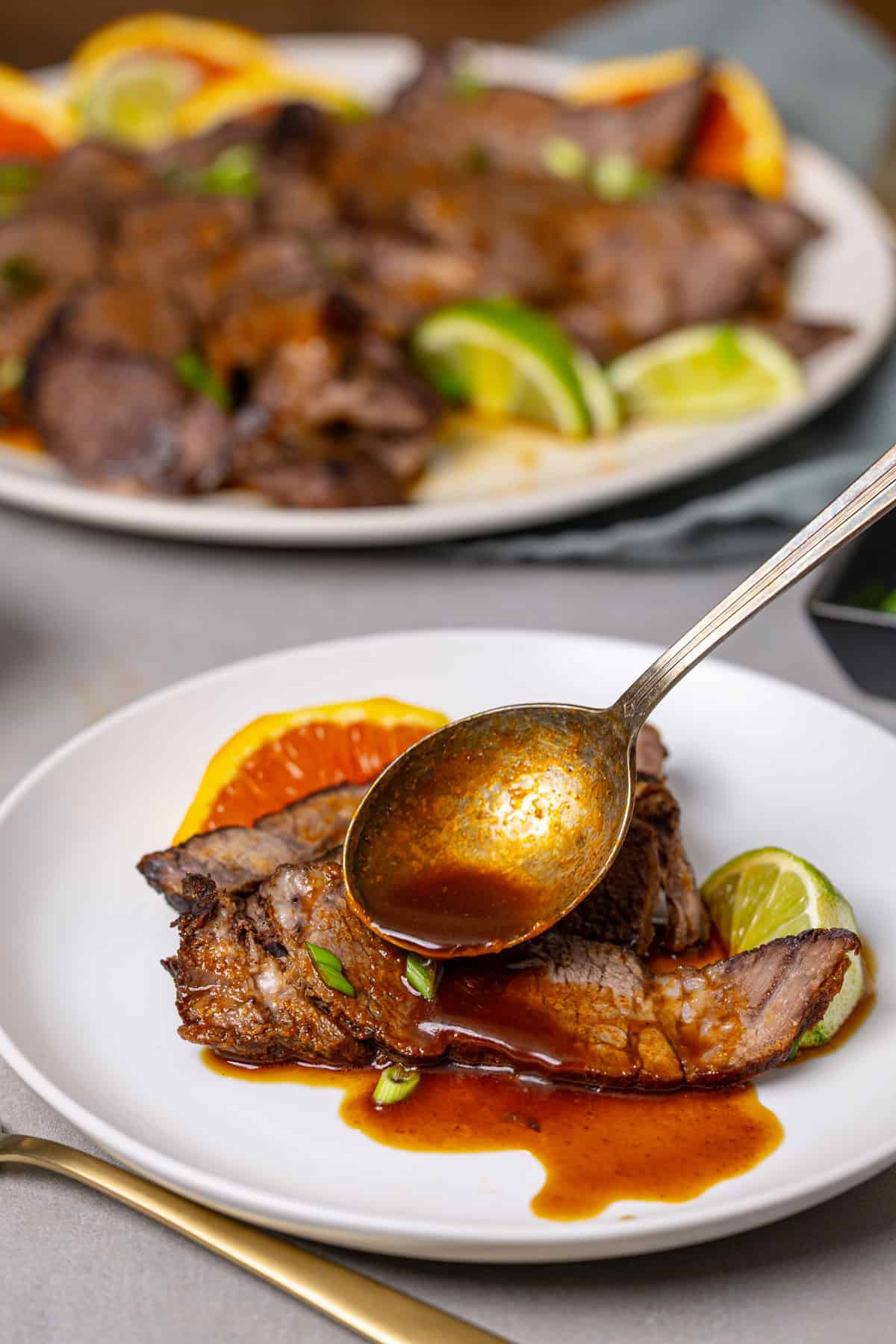 A close up of a plate of braised chuck roast with a spoon topping it with a brown sauce.