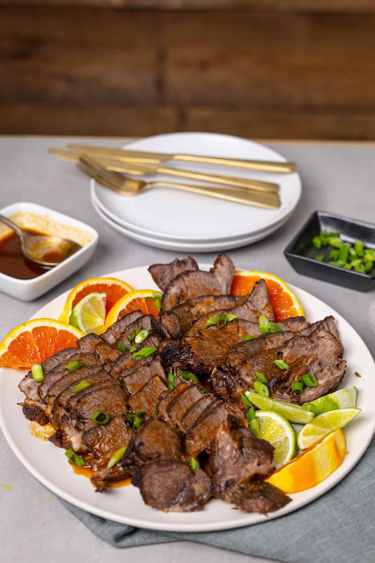 A platter of braised chuck roast with citrus on a grey table.