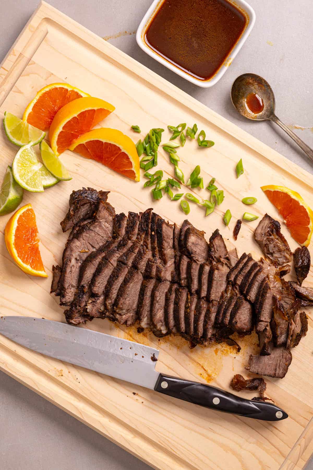 A cutting board with sliced of orange and lime, scallions, and braised chuck roast.