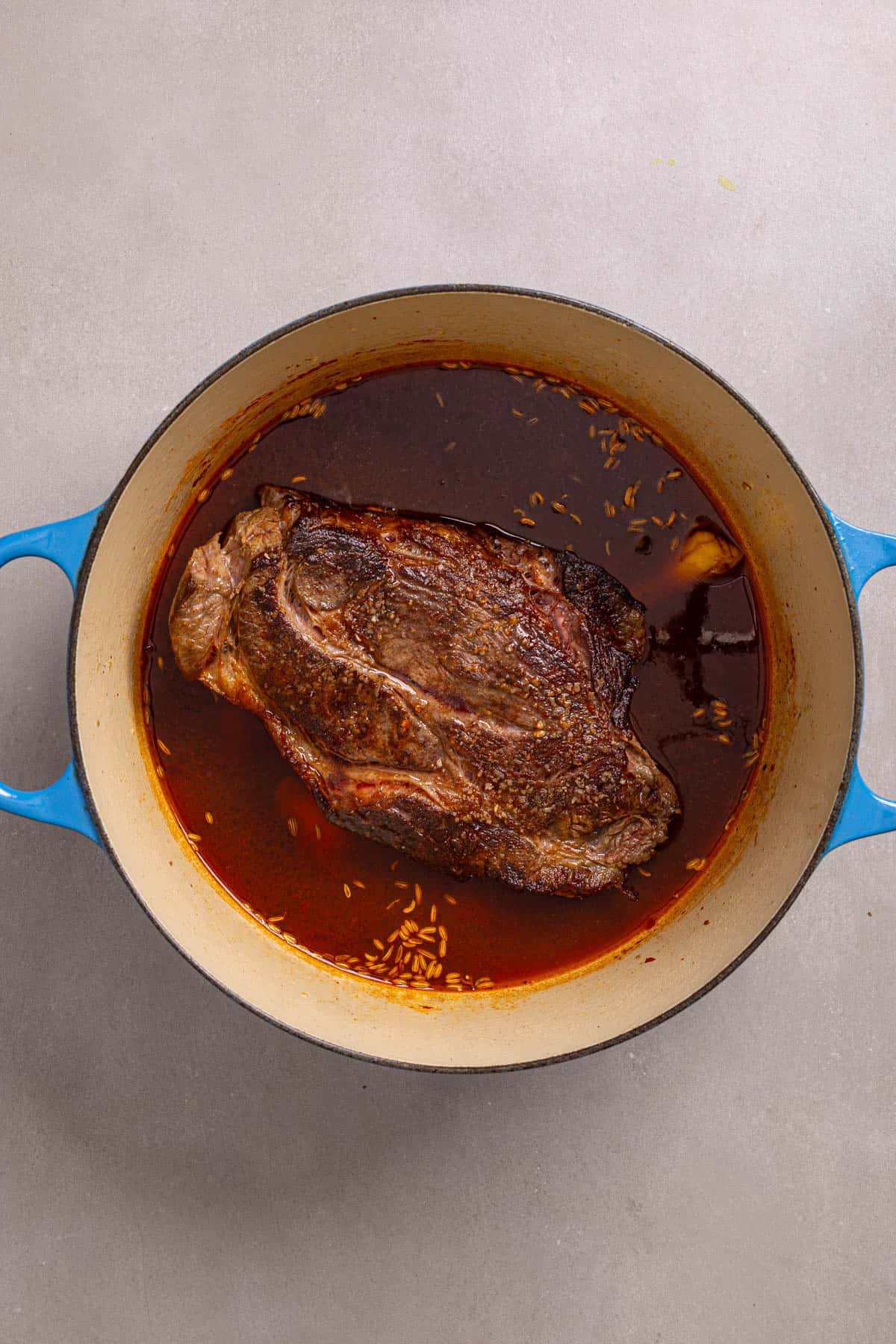 A Dutch oven with a browned chuck roast and braising liquid.