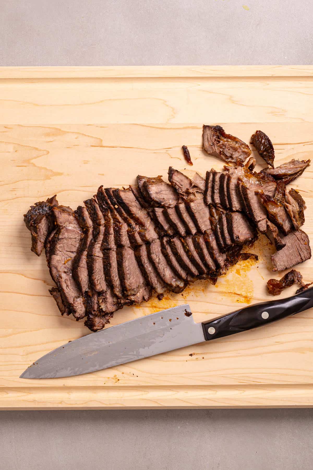 Braised chuck roast on a cutting board thinly sliced.