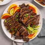 A close up of a platter with braised chuck roast sliced thin garnished with orange and lime.