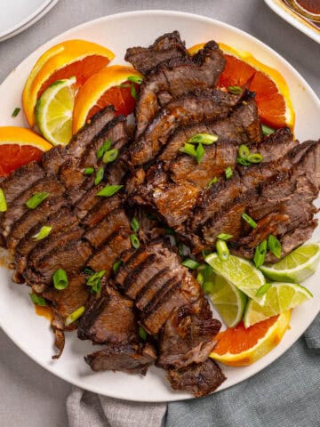 A close up of a platter with braised chuck roast sliced thin garnished with orange and lime.