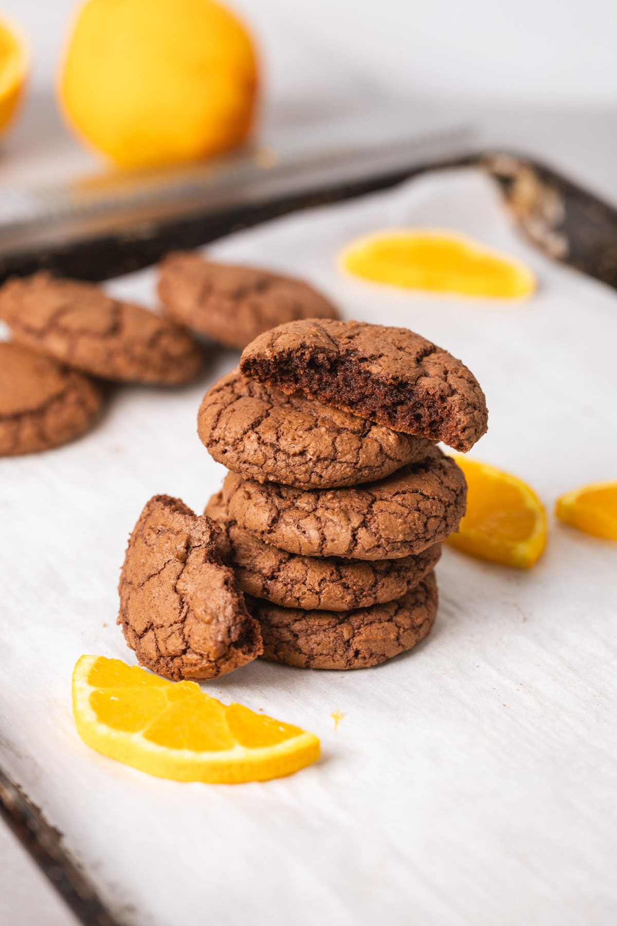 A stack of chewy chocolate and orange cookies on a parchment-lined baking sheet with slices of oranges as a garnish.