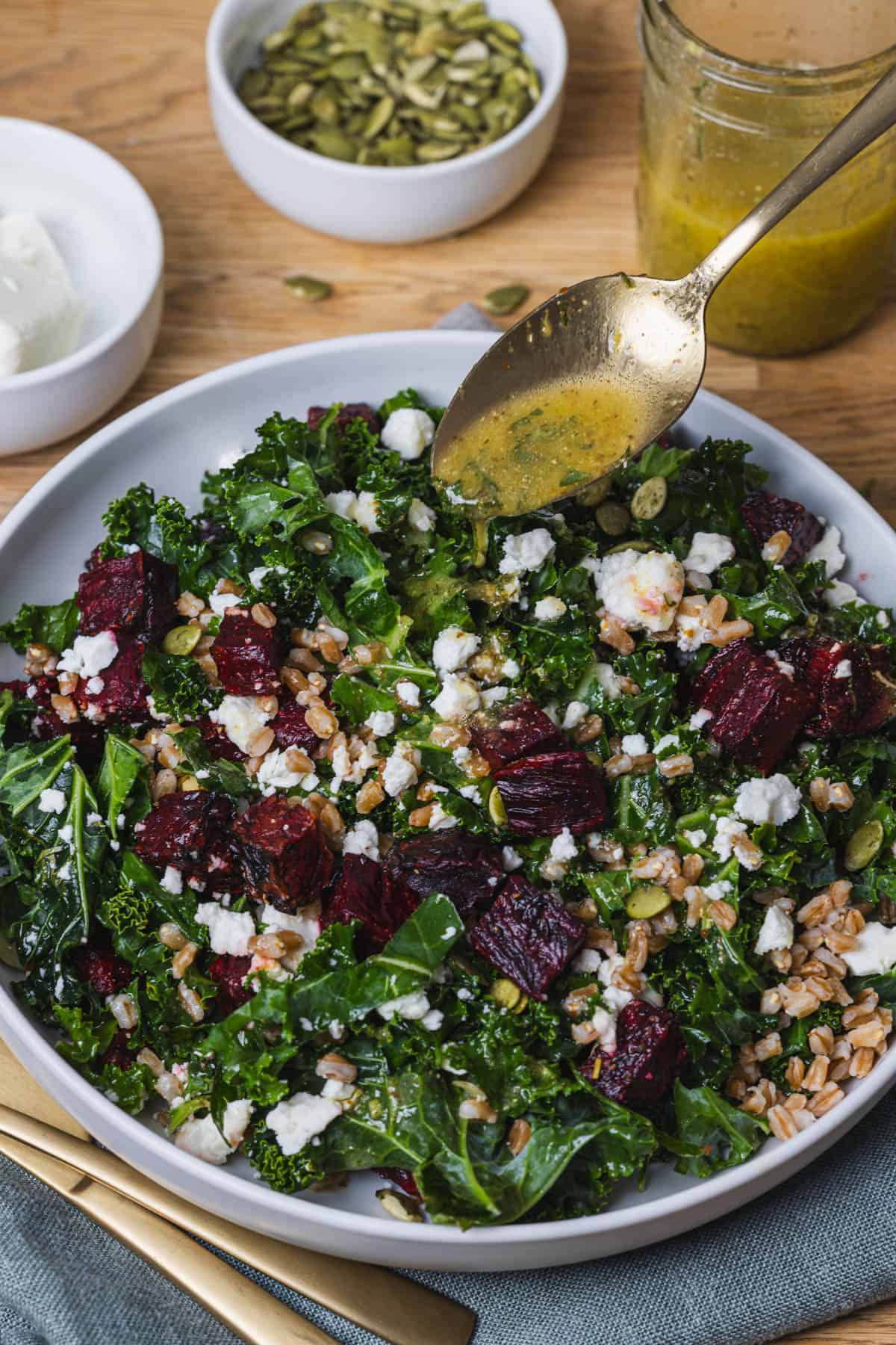 Lemon dressing getting spooned over a beet and kale salad with crumbed feta cheese and farro.