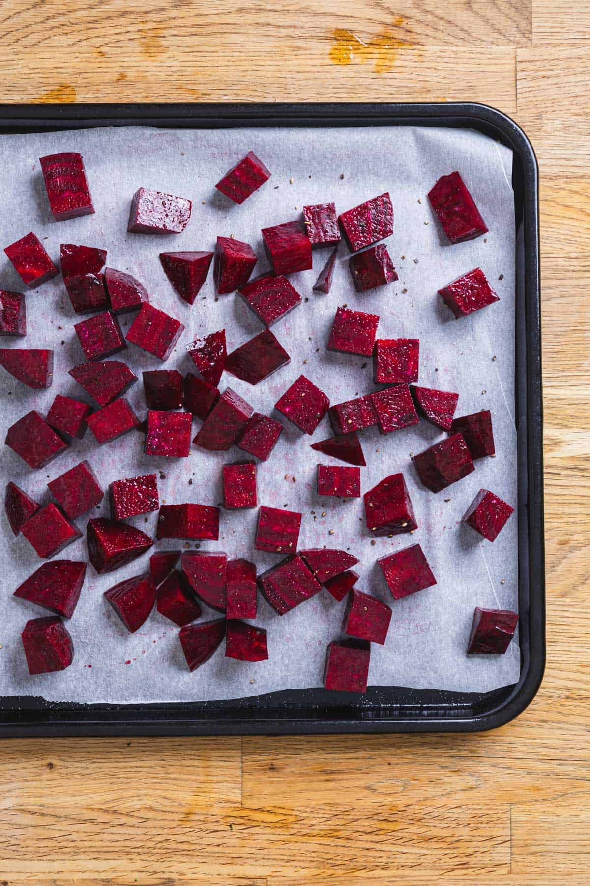 Chopped purple beets on a parchment-lined baked sheet.
