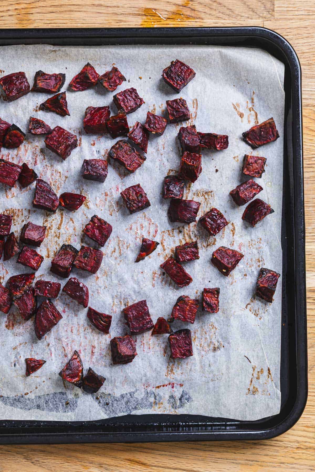 Roasted purple beets on a parchment-lined baking sheet.