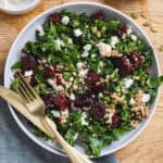 A serving bowl of beet and kale salad with farro and crumbled feta on a butcherblock counter.