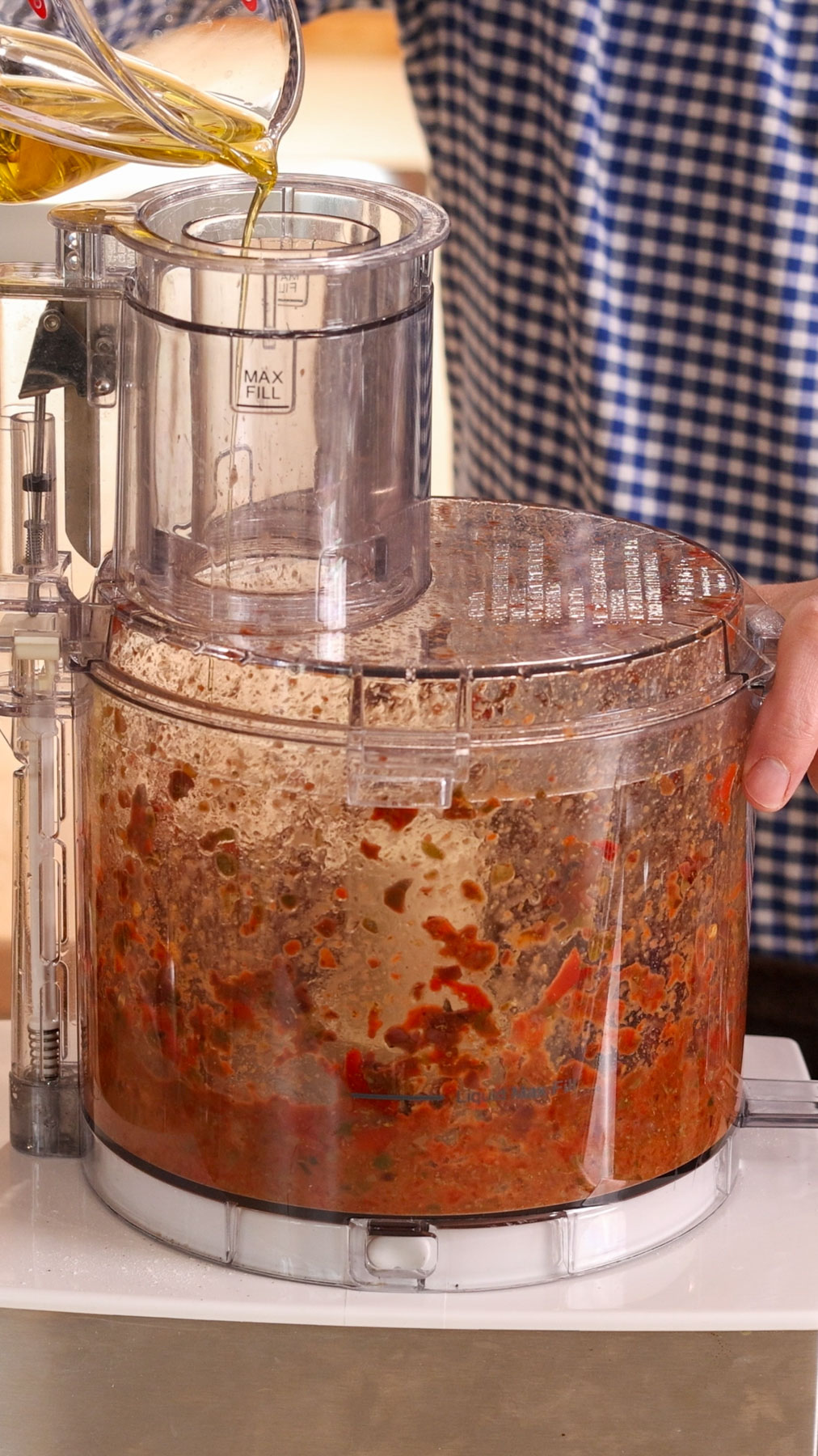 Oil slowly drizzling into a food chute of a food processor for a red pepper pantry pasta sauce.