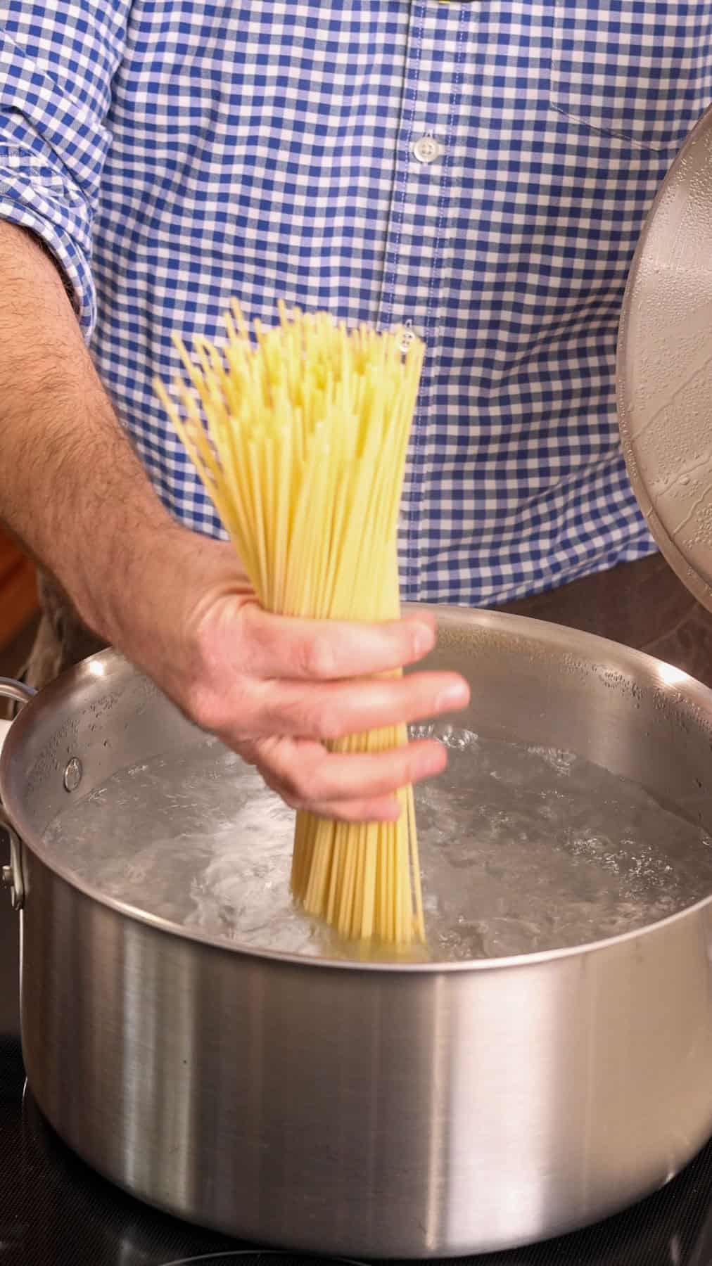 Spaghetti getting added to a large pot of boiling water.