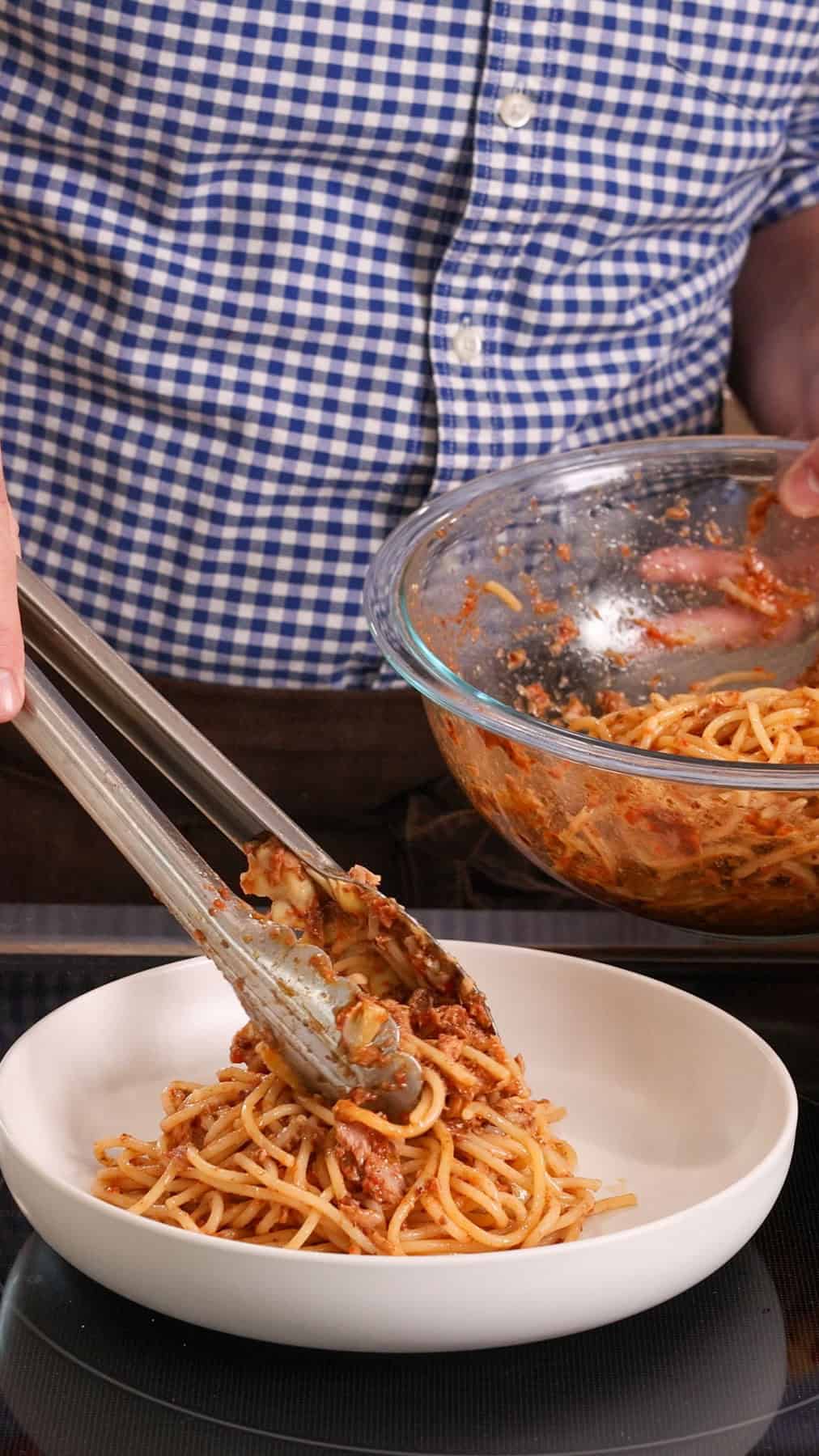 Pantry pasta with canned tuna getting plated in a white bowl.
