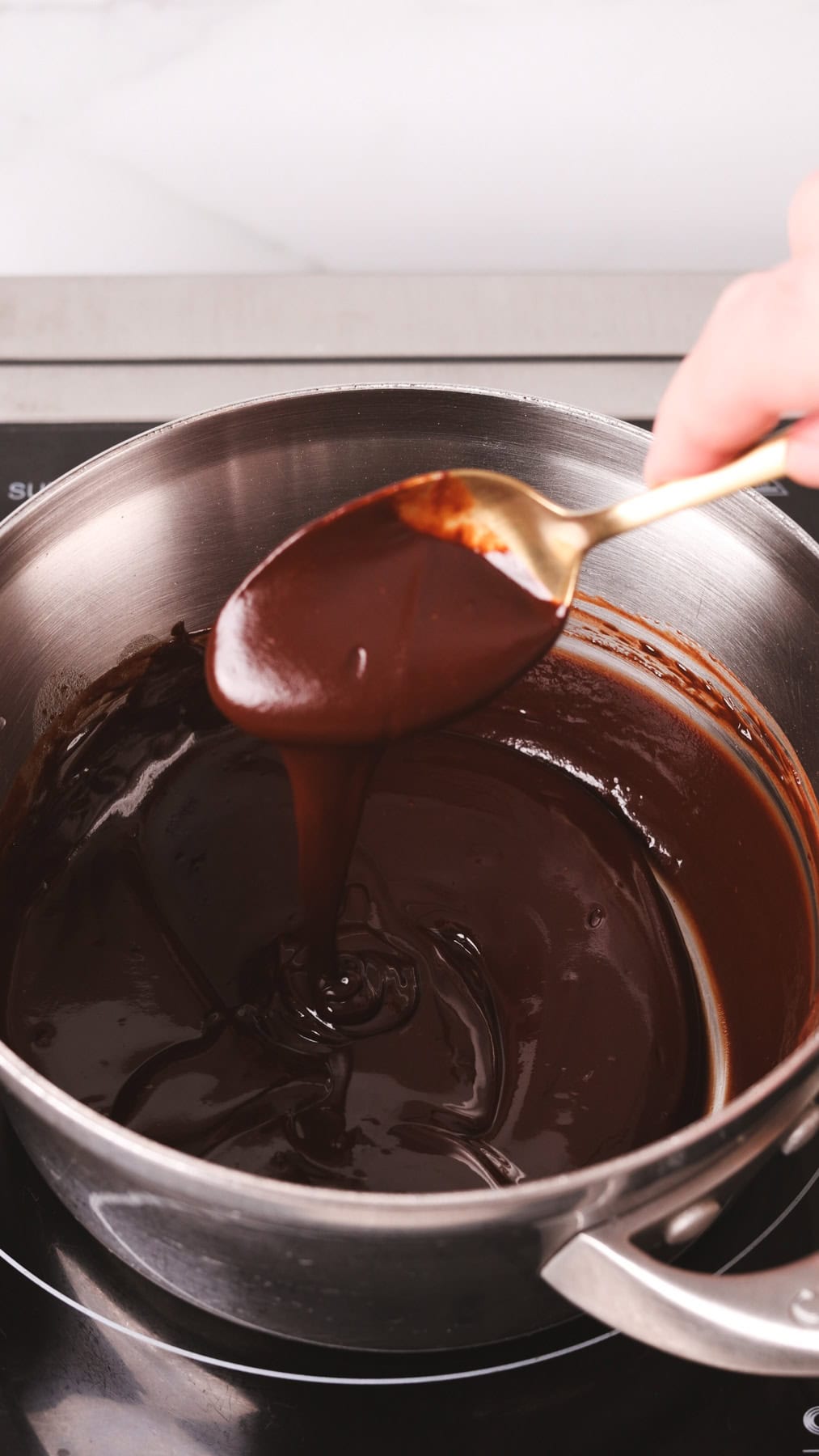 Chocolate melting in a small saucepan with a spoon showing off the smooth texture.