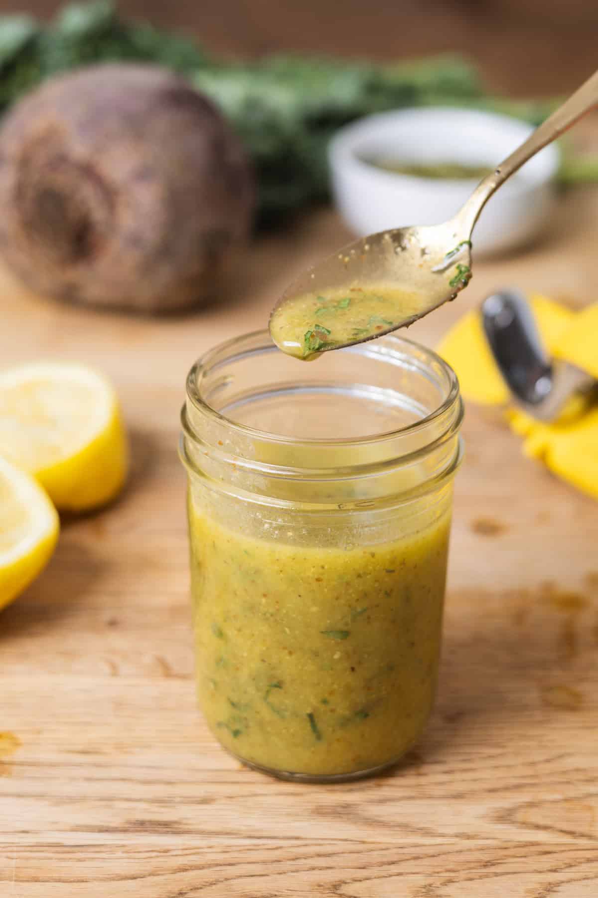 A small mason jar with lemon Dijon dressing on a butcherblock countertop.