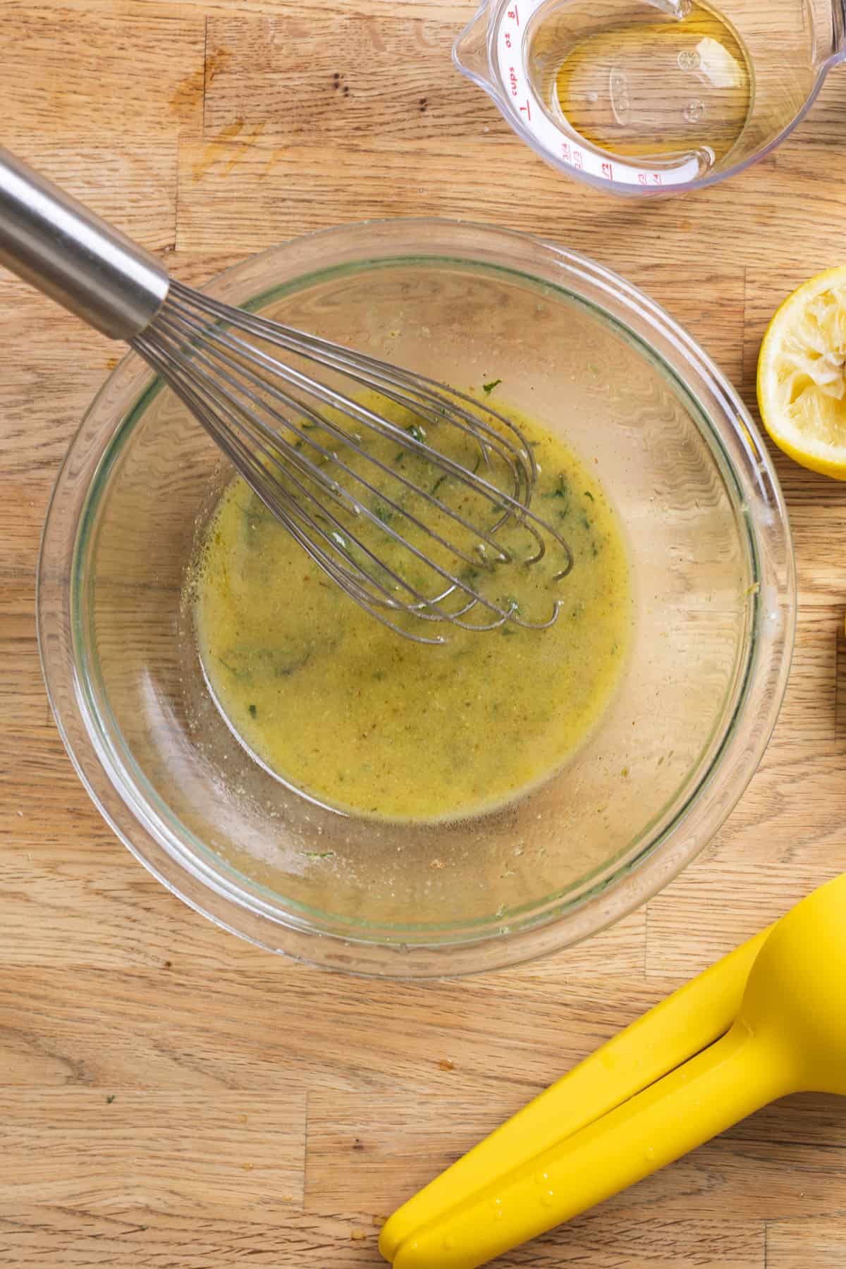 Lemon Dijon Dressing getting whisked together in a glass bowl on a butcherblock counter.