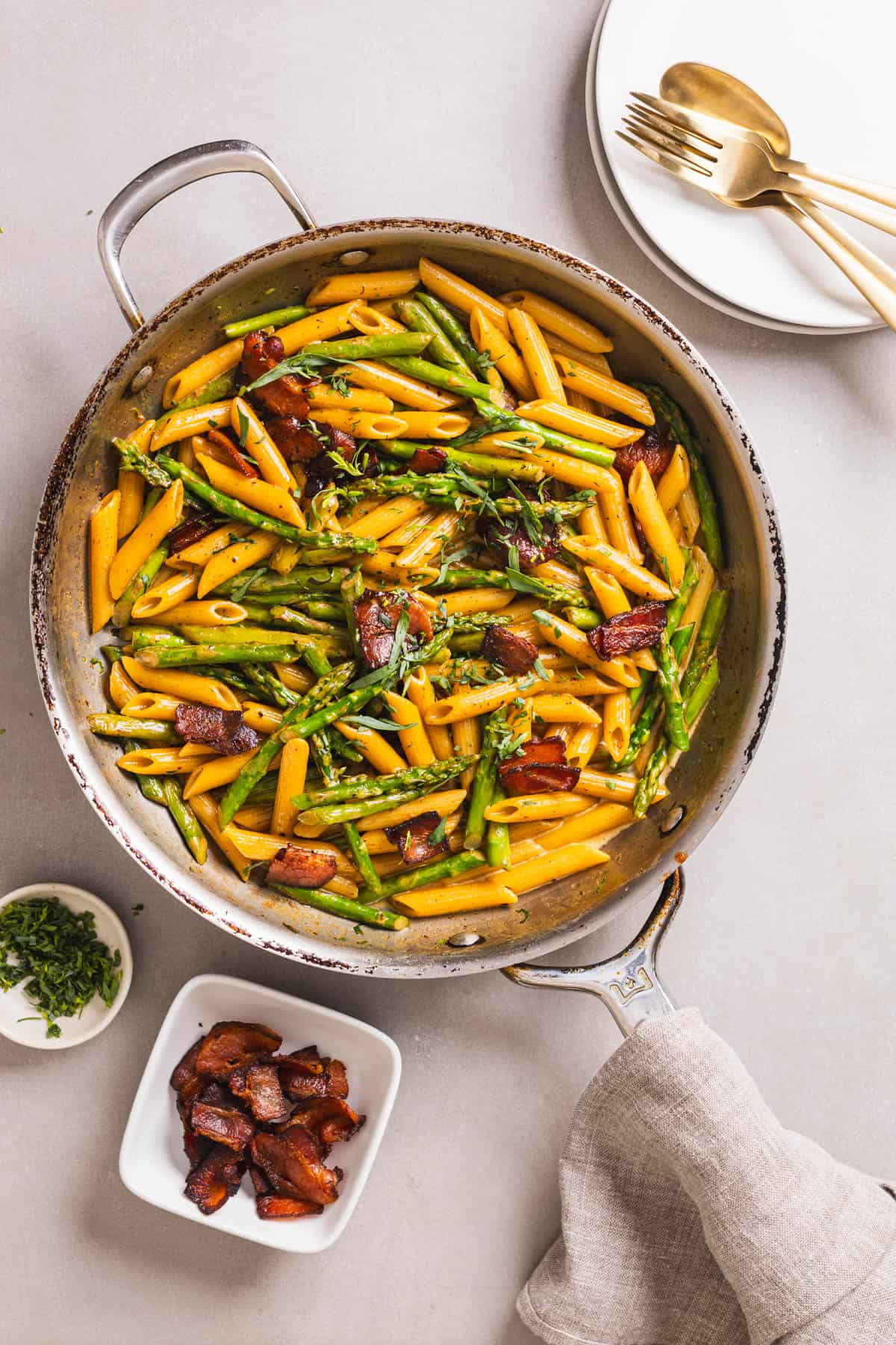 A skillet with bacon and asparagus pasta in a light cream sauce garnished with chopped tarragon.