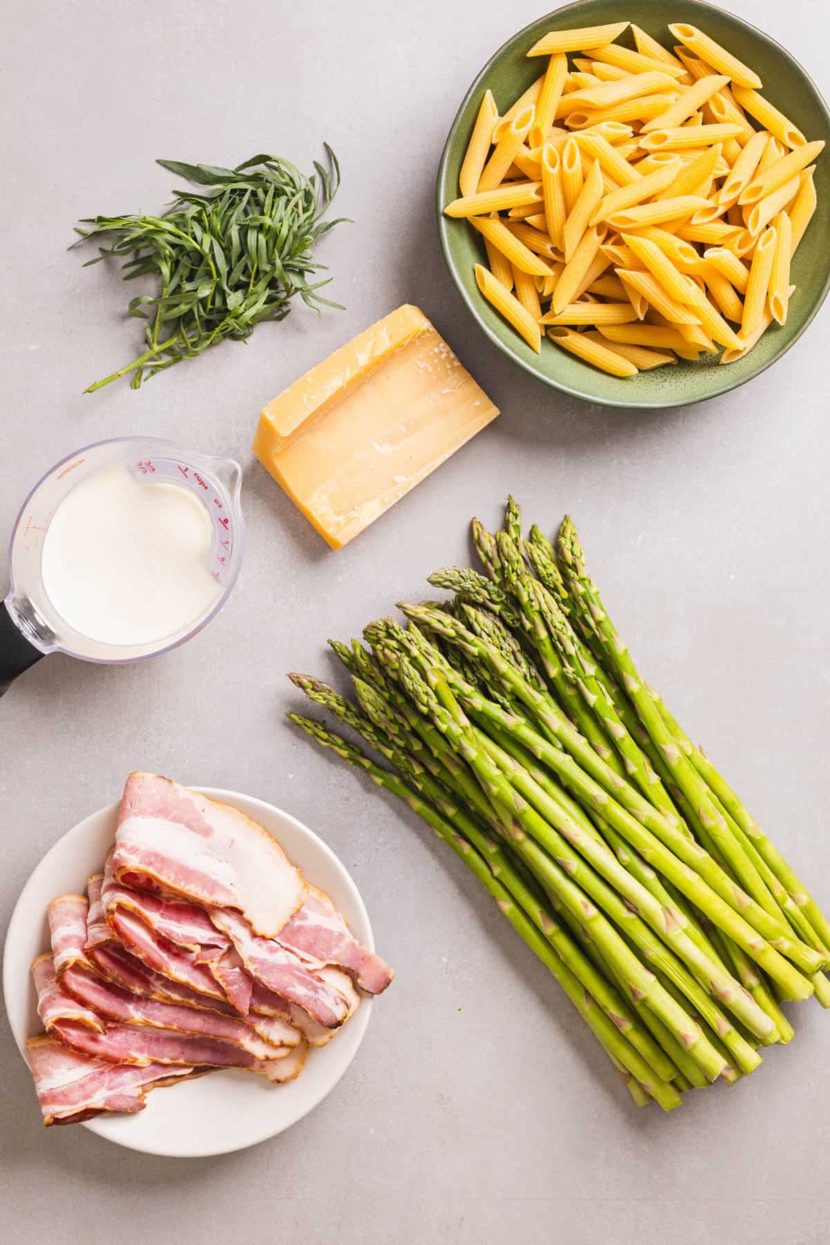 Ingredients for bacon and asparagus pasta on a gray table.