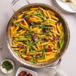 A close-up shot of a skillet with bacon and asparagus pasta garnished with fresh tarragon.